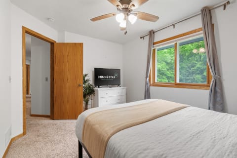 A well-lit bedroom with a window and a modern television.