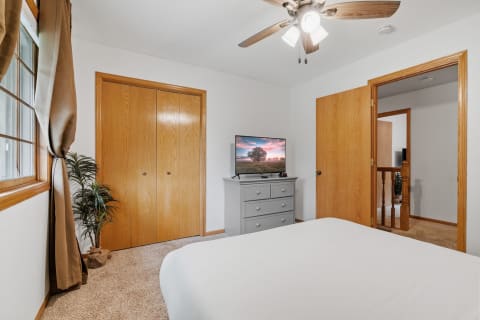 A serene bedroom with a gray dresser, flat-screen TV, and wooden doors.