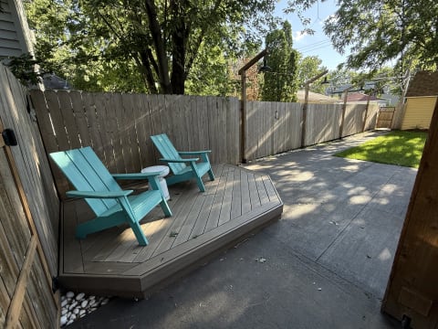 Turquoise Adirondack chairs on a wooden deck next to a small table in a backyard setting.