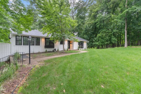 Single-story home surrounded by greenery with a pathway leading to the entrance.