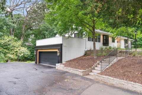 A contemporary house with a black garage, stone stairs, and green trees around it.