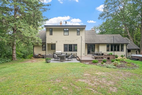 Back view of a house with a deck, outdoor seating, and greenery.